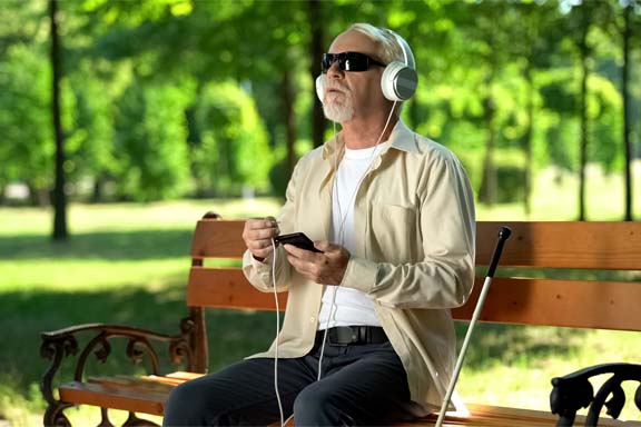 Old blind man putting headset cable in phone, listening voice me